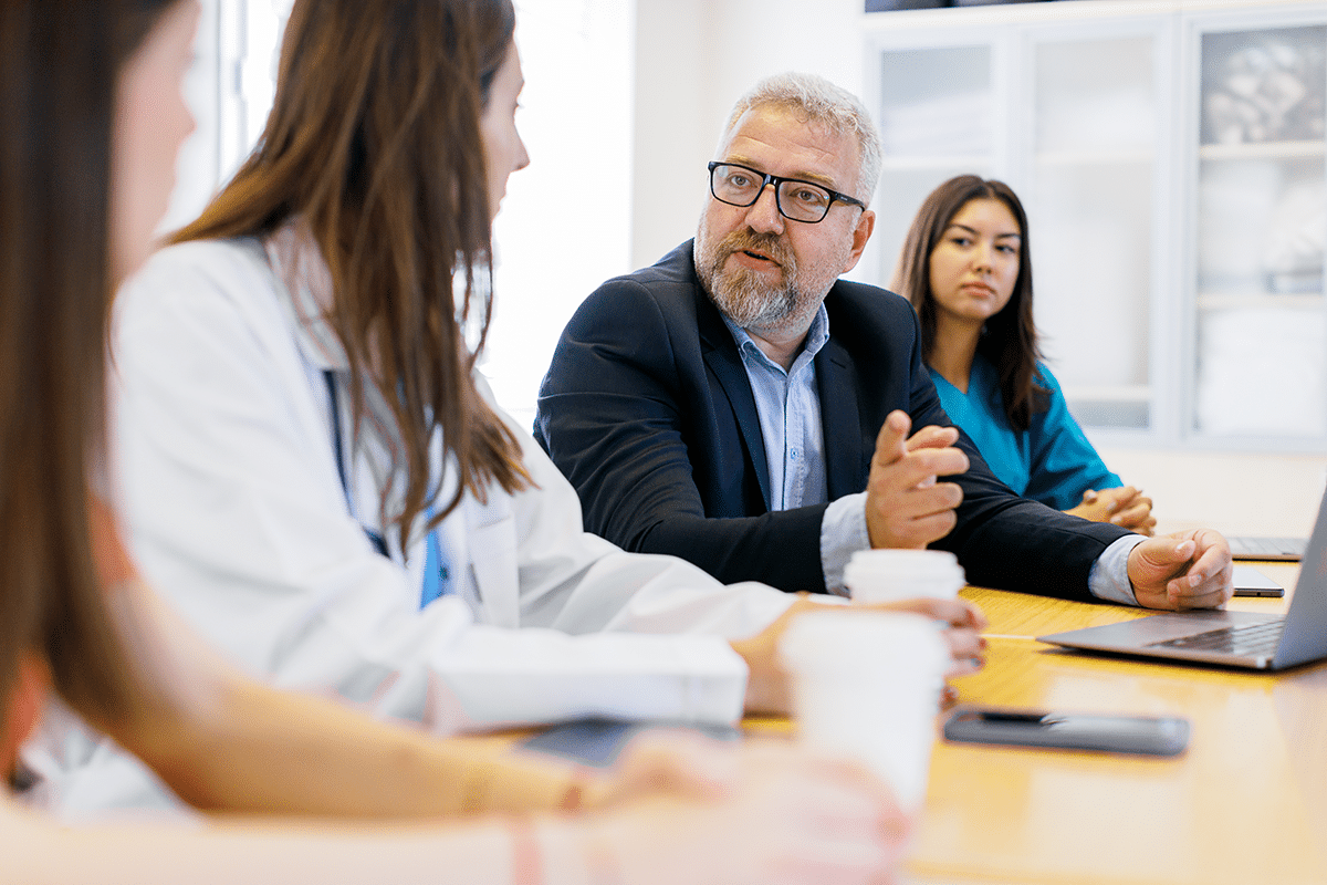 man in suit at conference table with physicians in active discussion on interoperability