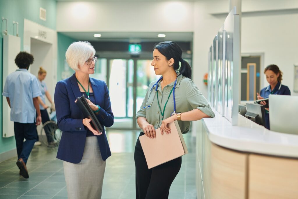 An administrator and a physician discuss provider data accuracy near the reception desk.