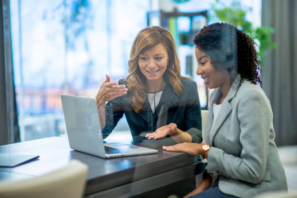 Two data stewards discuss identity governance while reviewing a laptop screen.